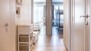 A narrow hallway with a wooden floor, a white bench, and a door on the right. - Kentucky 603 (Koksijde)