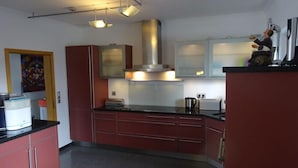 Una cucina moderna con mobili rossi, elettrodomestici in acciaio inossidabile e lampade a sospensione.