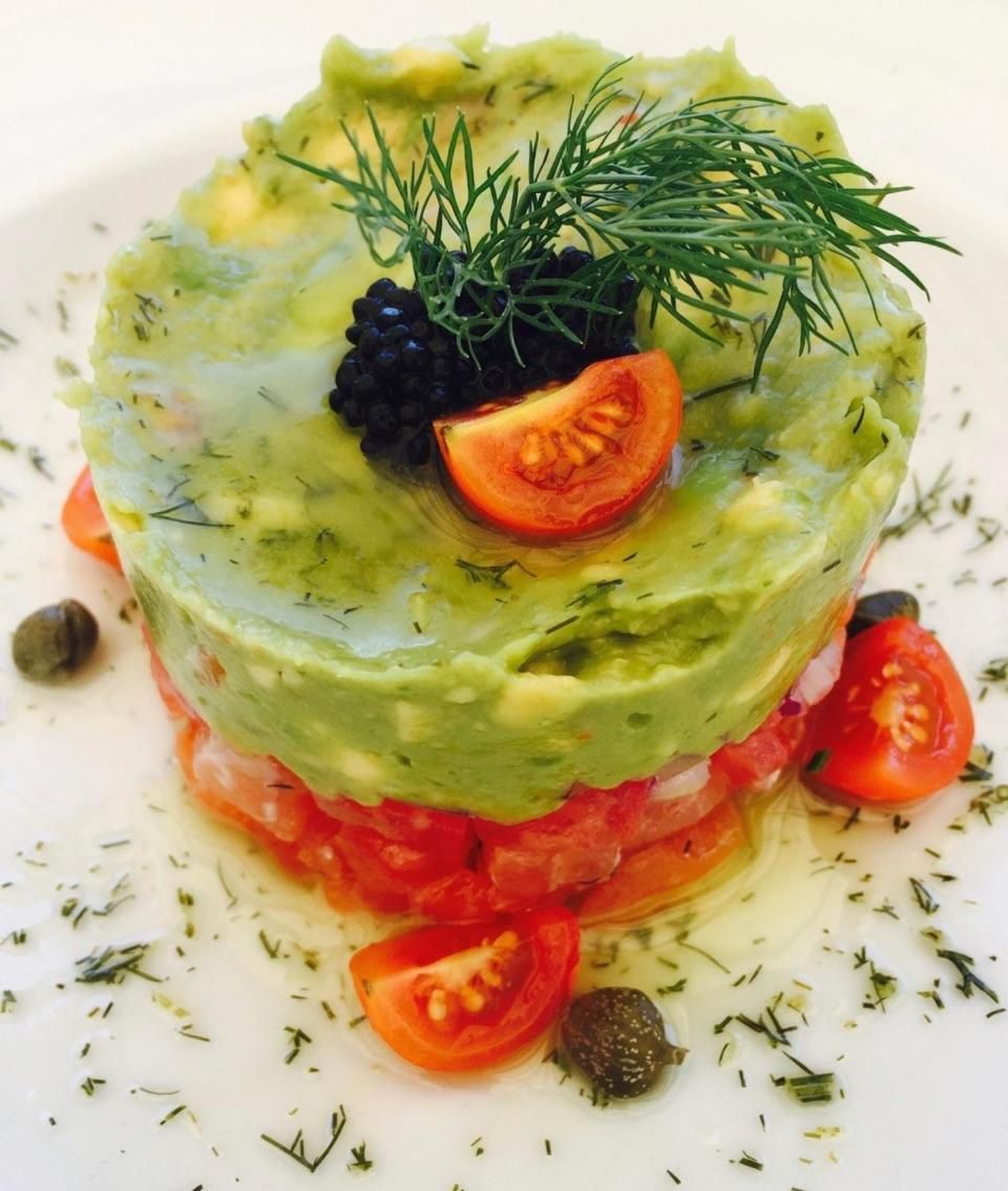 Une salade composée de couches d’avocat, de tomates et de mûres, présentée dans une assiette blanche.