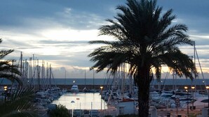 A marina at dusk with boats docked, palm trees, and a calm sea. - Hotel Playa Canet (Canet de Berenguer)