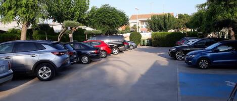 Un estacionamiento con varios autos estacionados, rodeado de árboles y edificios.