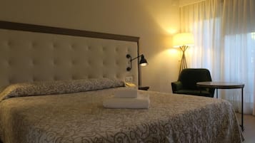 Una habitación de hotel con una cama grande, una silla, una mesita y una lámpara.