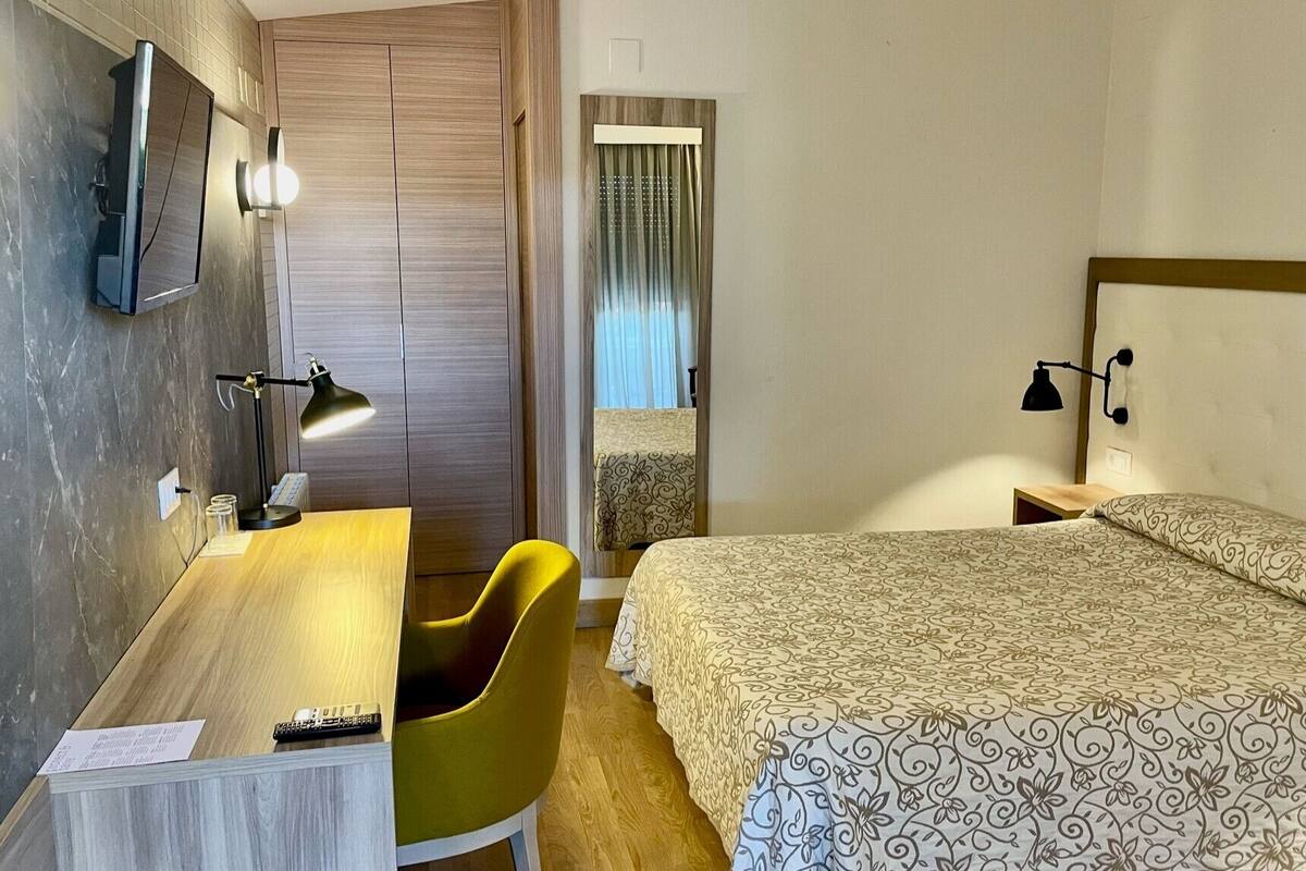 A hotel room with a bed, a desk, a chair, and a TV.