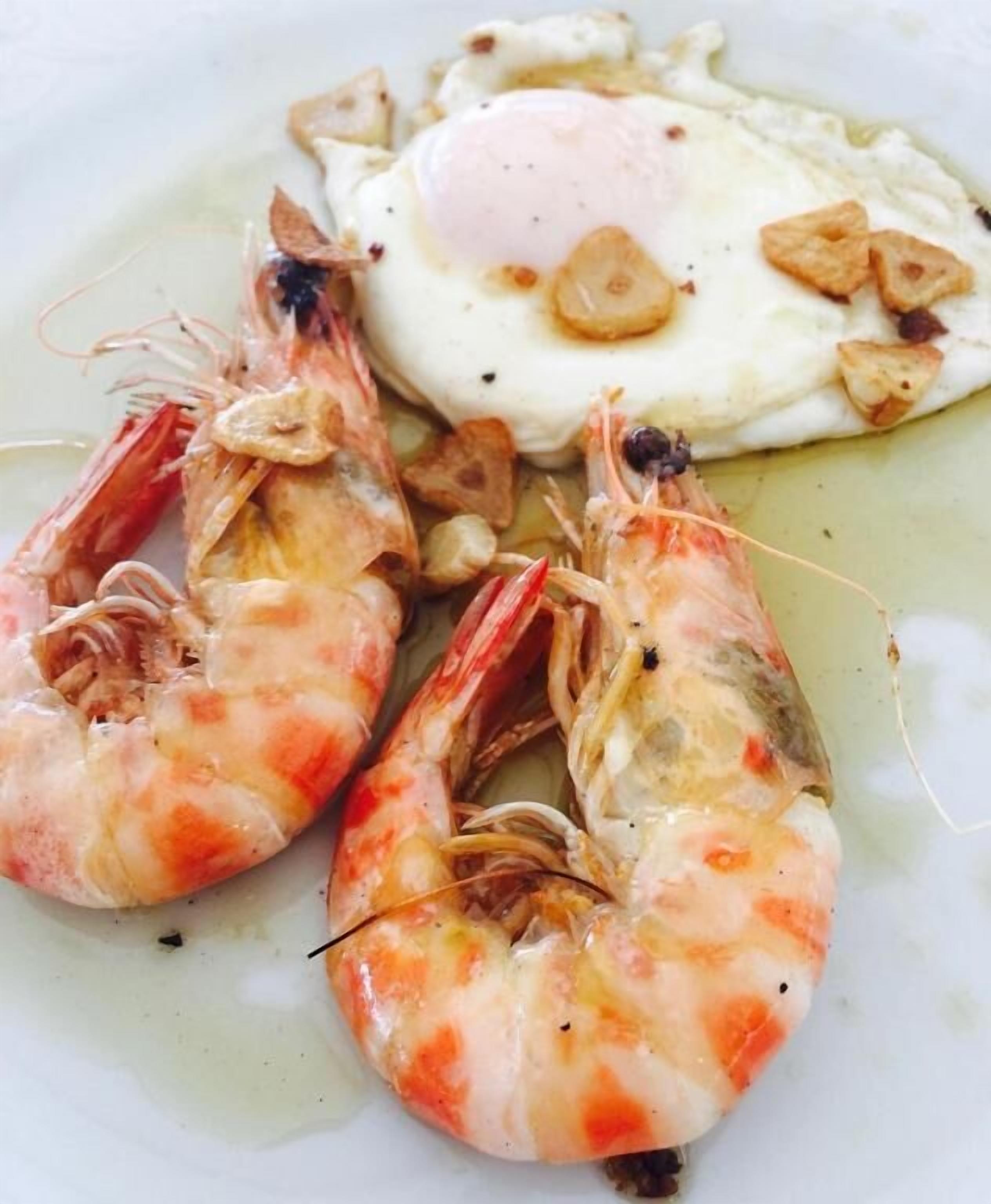 A plate with cooked shrimp and a fried egg.
