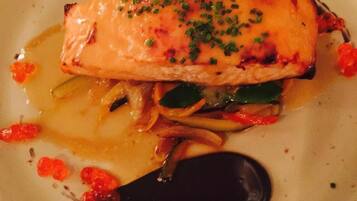 A plate with a piece of salmon, vegetables, and a dark sauce.