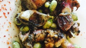 A close-up of a dish with octopus and green beans, seasoned with herbs and spices.
