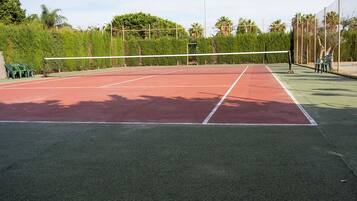 An outdoor tennis court with a net, surrounded by greenery and trees.