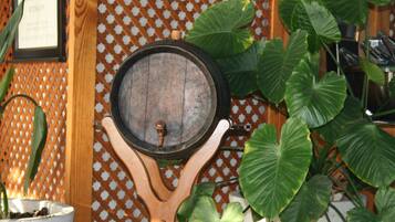 A wooden barrel mounted on a decorative stand with a metal latch, surrounded by large green leaves.
