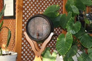 A wooden barrel mounted on a decorative stand with a metal latch, surrounded by large green leaves.
