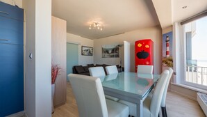 A modern living room with a glass dining table, white chairs, a blue cabinet, and a red decorative piece. - San Remo 501 (Koksijde)
