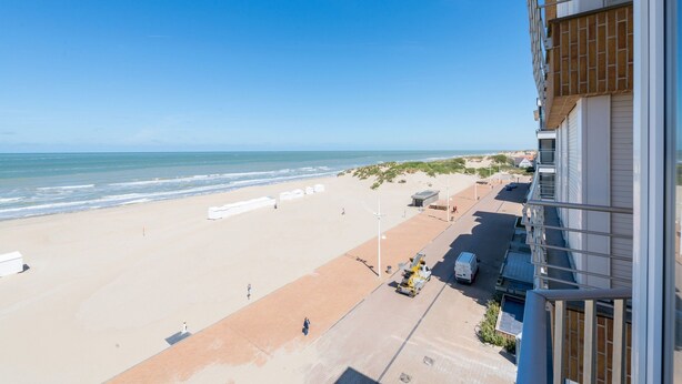 A beach view from a building with a paved walkway leading to the shore, a parked van, and a lifeguard tower. - San Remo 501 (Koksijde)