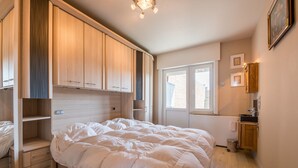 A bedroom with a large bed, built-in wooden wardrobe, a small window, and a bedside table. - San Remo 501 (Koksijde)