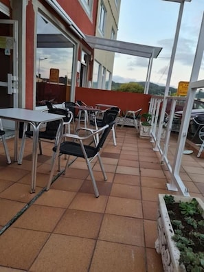 An outdoor patio with metal tables and chairs, a covered seating area, and a view of the surrounding landscape. - Hospedaxe Don Manuel (O Vicedo)