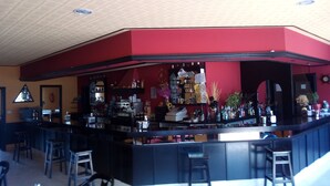 A bar area with a red accent wall, bar stools, and a variety of bottles and glasses on shelves. - Hospedaxe Don Manuel (O Vicedo)
