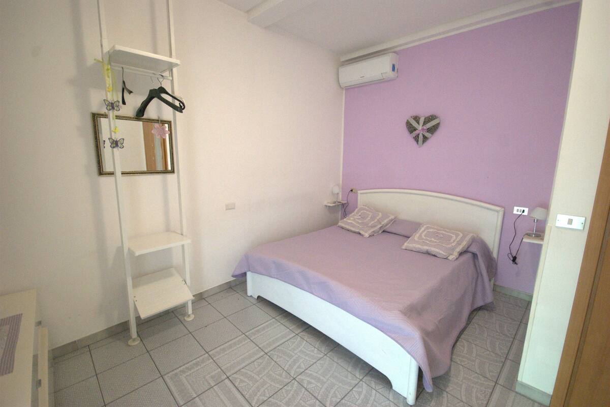 A bedroom with a bed, a white shelf unit, and a wall-mounted air conditioner.