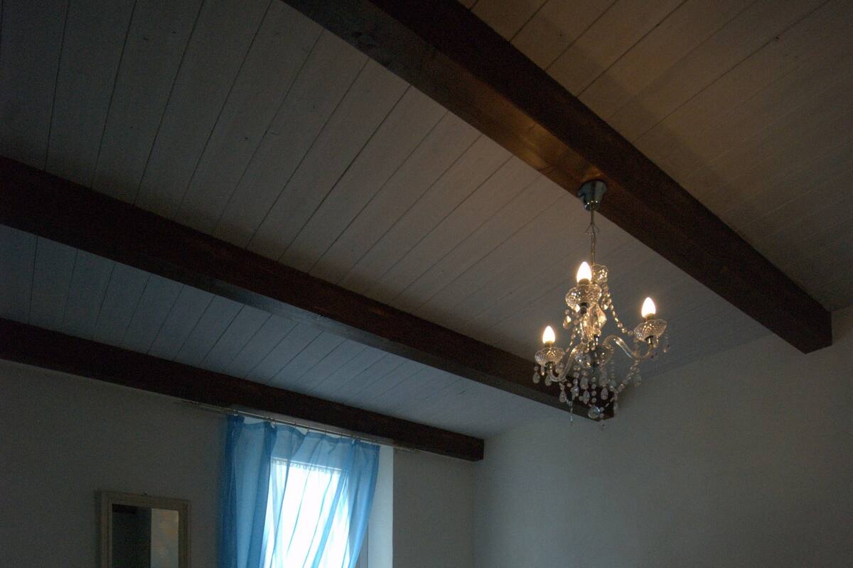 A bedroom with bunk beds, a chandelier, a window with blue curtains, and a mirror on the wall.