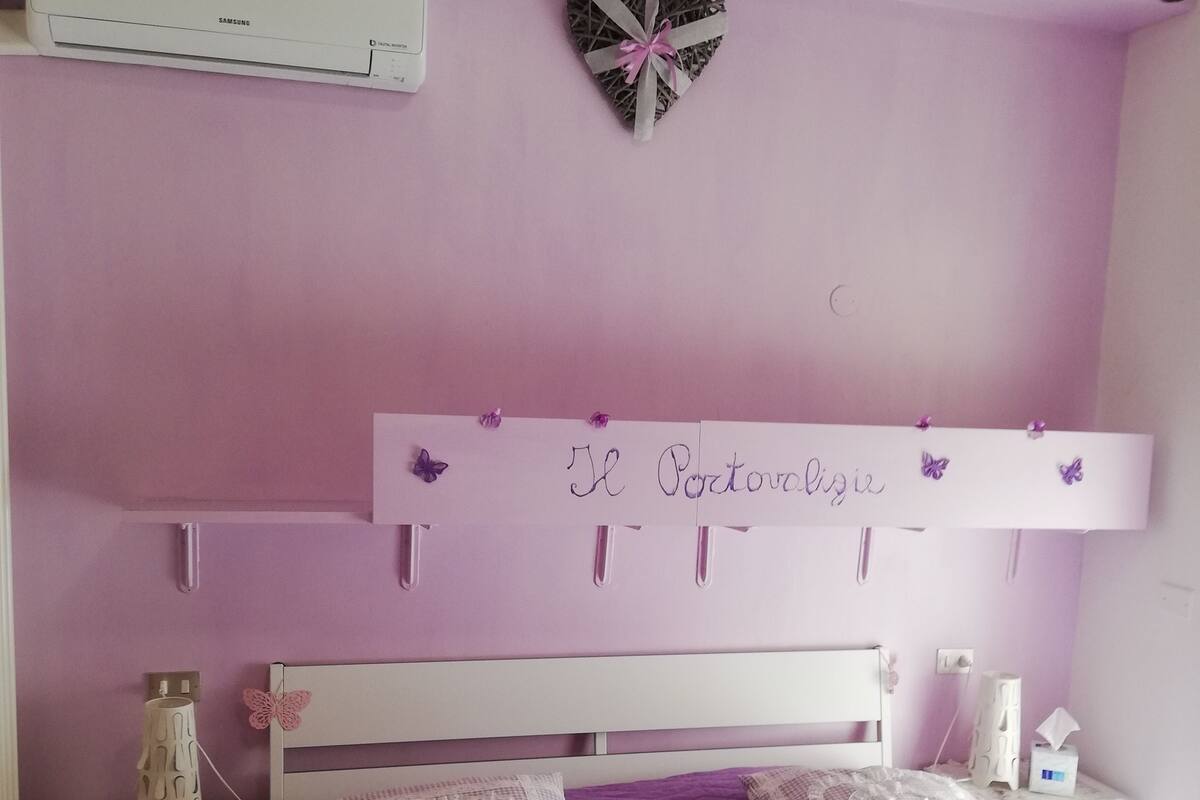 A bedroom with a purple bedspread, a white headboard, and a wall-mounted shelf with decorative items.