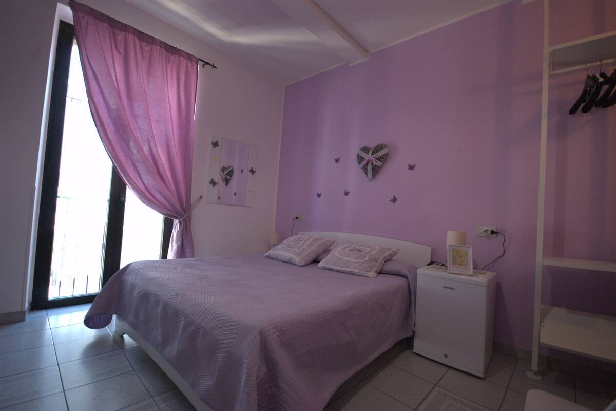 A bedroom with a bed, a nightstand, a dresser, and a window with curtains.