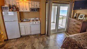 A compact kitchen with a refrigerator, stove, and microwave. There is a sliding glass door leading to a balcony with a view of the ocean. - Florence I 608 Minium Studio Bedroom Condo by RedAwning (South Padre Island)