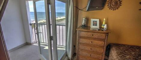 Ein Zimmer mit einer Schiebeglasdoor, die auf einen Balkon mit Blick auf den Strand führt.