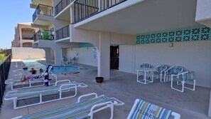 A poolside area with lounge chairs, a pool, and a building with balconies.