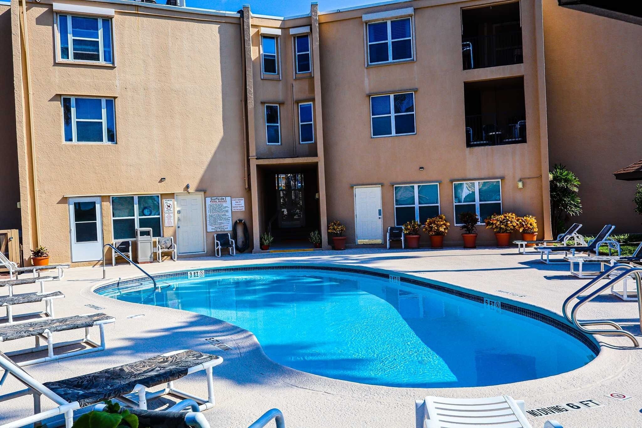A swimming pool with lounge chairs and a building with multiple windows and balconies.