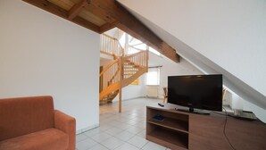 A living room with a TV on a wooden stand, a sofa, and a staircase leading to an upper level. - Hotel am Wasen (Freiberg am Neckar)