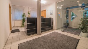 A reception area with a glass door, a reception desk, a potted plant, and a tiled floor. - Hotel am Wasen (Freiberg am Neckar)