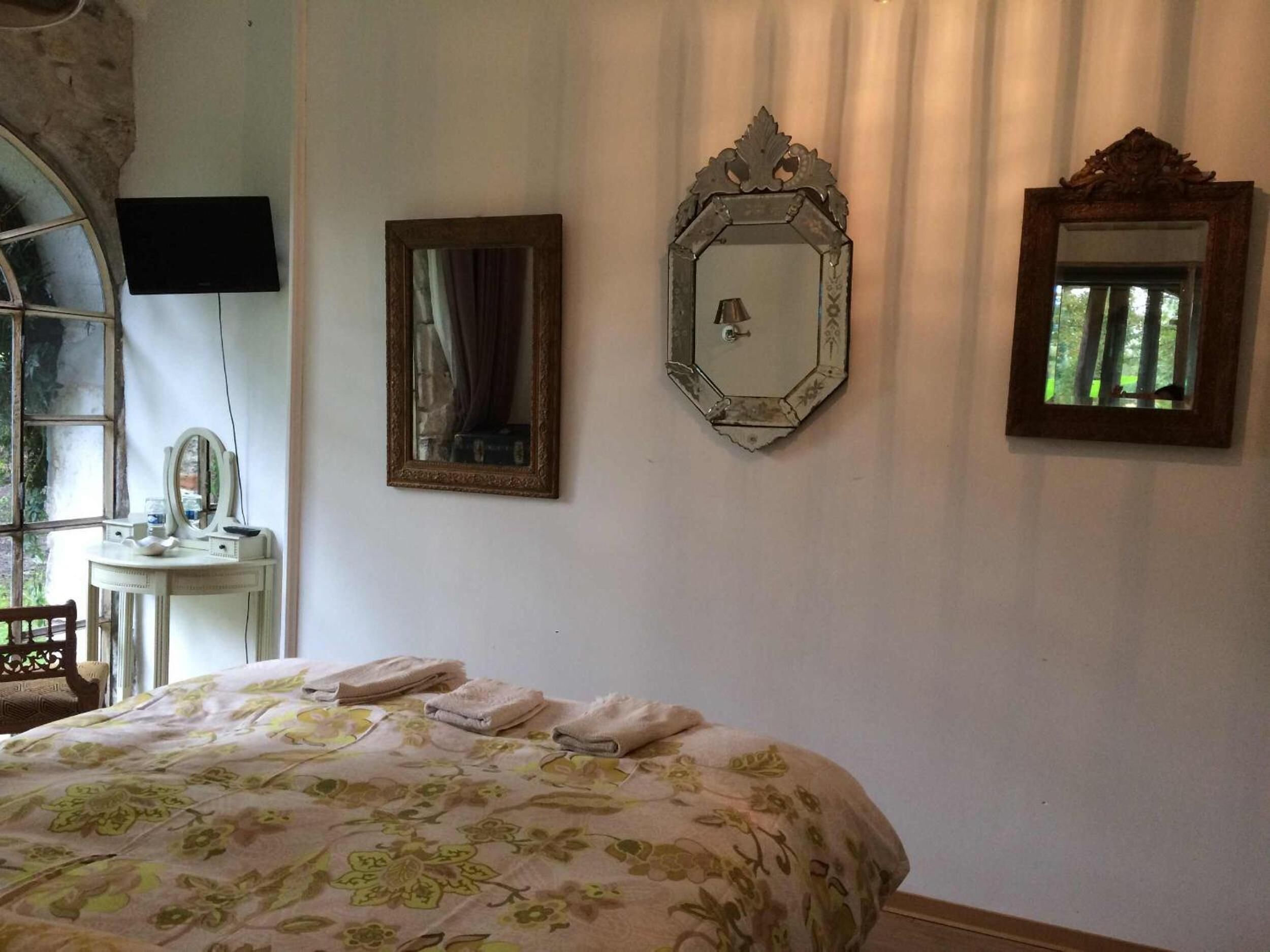 A bedroom with a bed, a vanity with a mirror, and two wall-mounted mirrors.