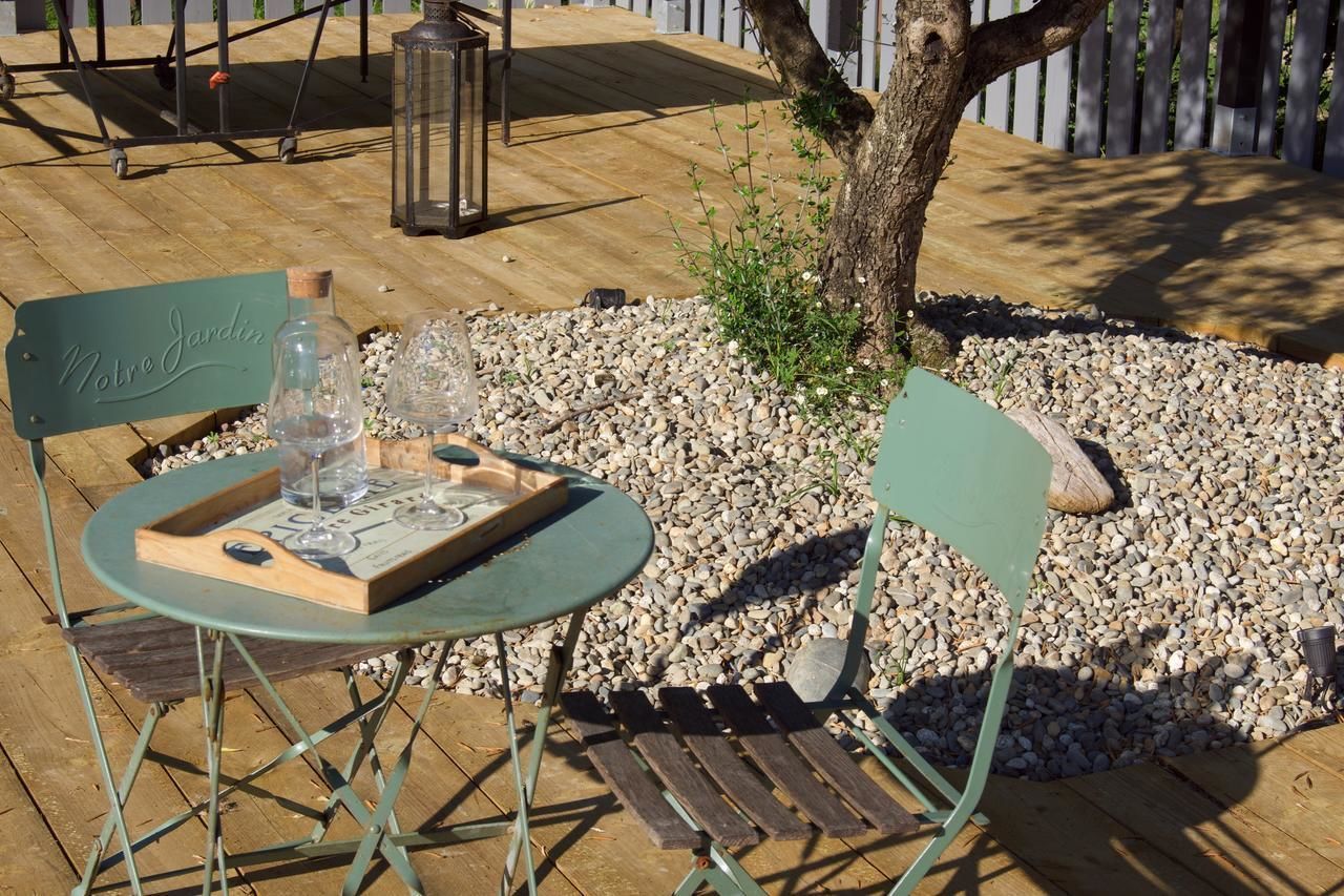 A wooden deck with a table and chairs, a lantern, and a sign that reads "Notre Jardin".