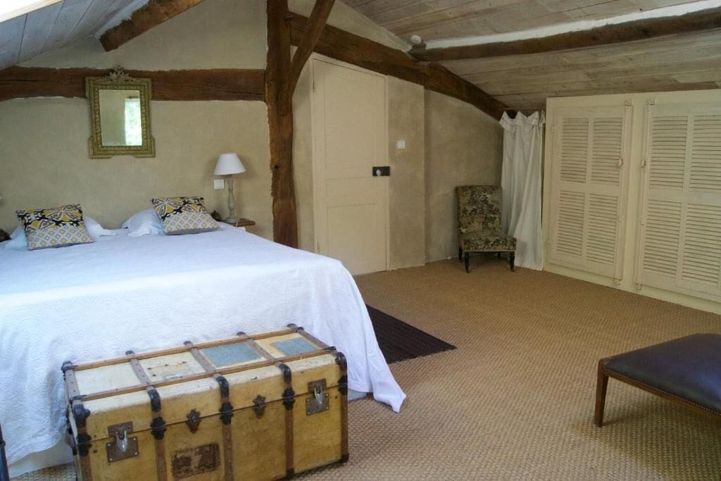 Un dormitorio con una cama, un cofre de madera, una silla y un armario.
