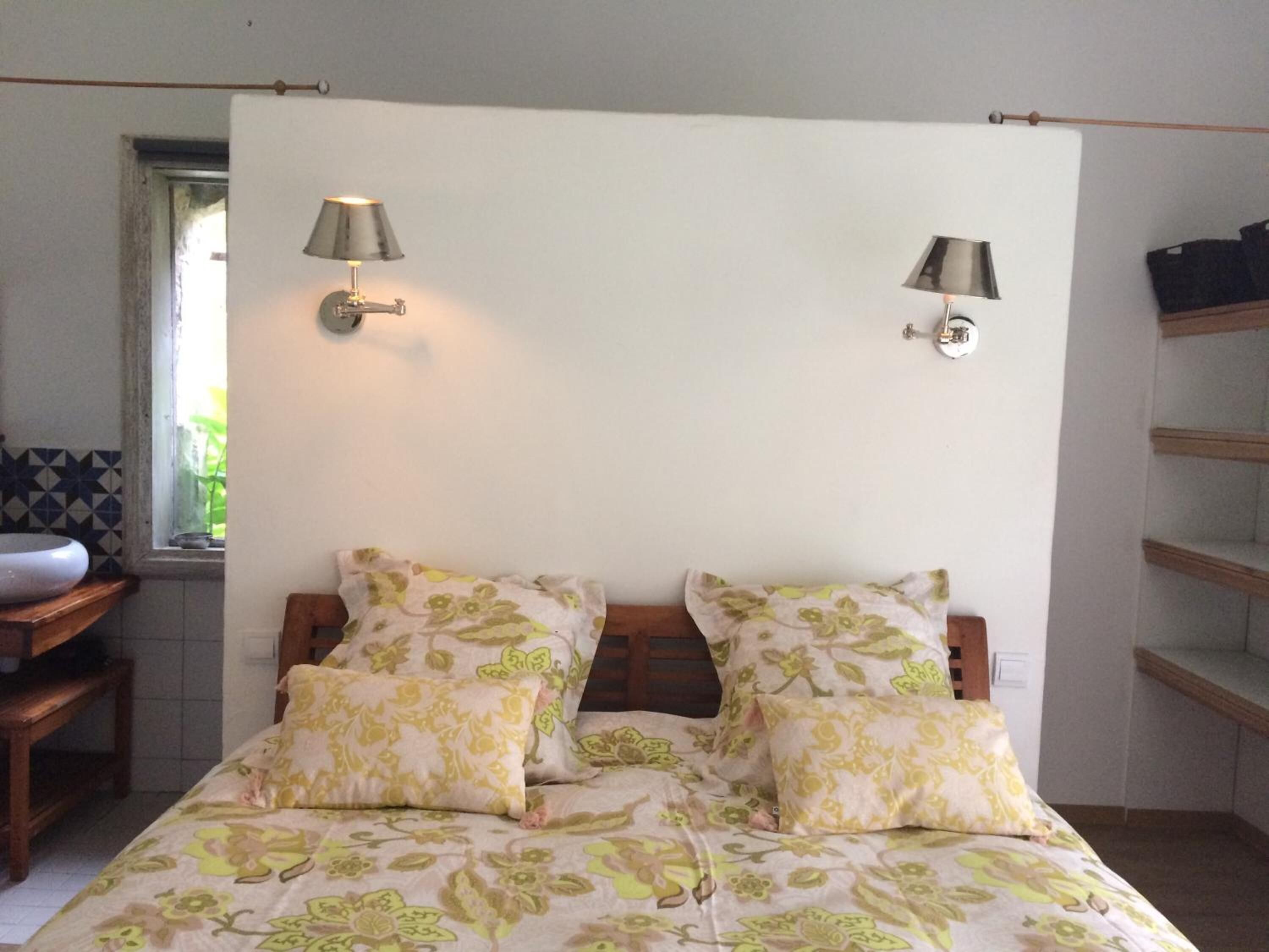 Une chambre à coucher avec un lit, deux lampes fixées au mur, une fenêtre et une petite table sur laquelle se trouve un bol.