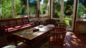 A sunlit room with a wooden table, wicker chairs, and a bench with red cushions. - Maison Basta (Orthevielle)