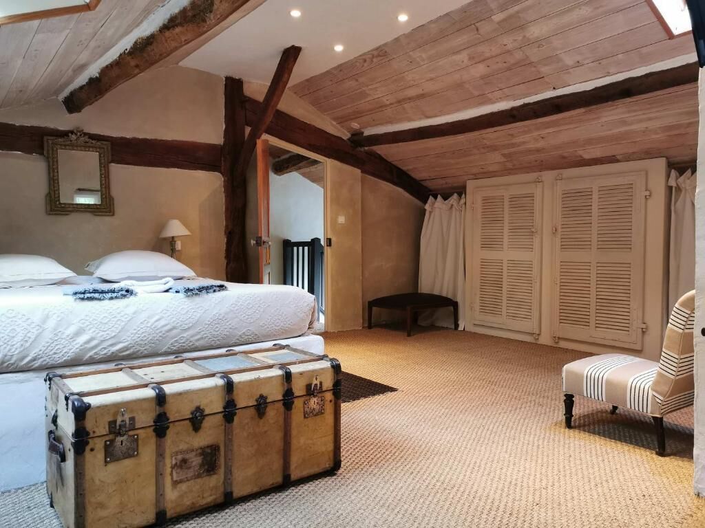 A bedroom with a large bed, a wooden ceiling, a suitcase, a chair, and a wardrobe.