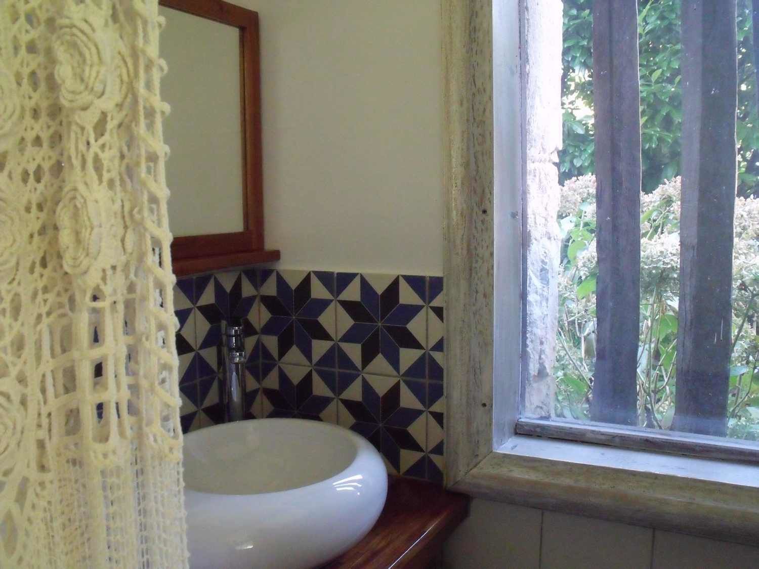 A bathroom with a white sink, a geometric patterned backsplash, a wooden countertop, and a window with a view of greenery.