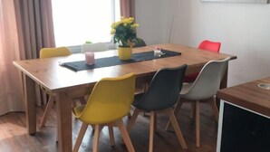A dining area with a wooden table, yellow and gray chairs, a small potted plant, and a painting on the wall. - Haus Strandoase (Behrendorf)