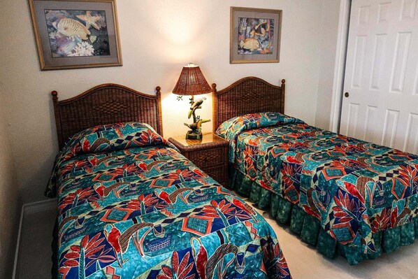 Una habitación con dos camas individuales, cada una con una colcha colorida, una mesita de noche con lámpara y cuadros en las paredes.
