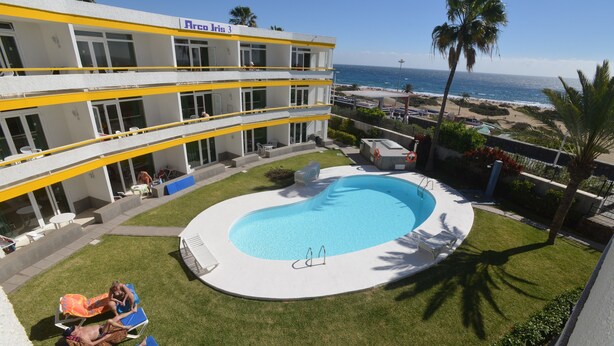 A hotel with a pool, outdoor seating, and a view of the ocean. - Apartamentos Arco Iris (San Bartolomé de Tirajana)