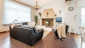 A living room with a fireplace, a sofa, a TV, and a dining area. - Marsouins (Koksijde)