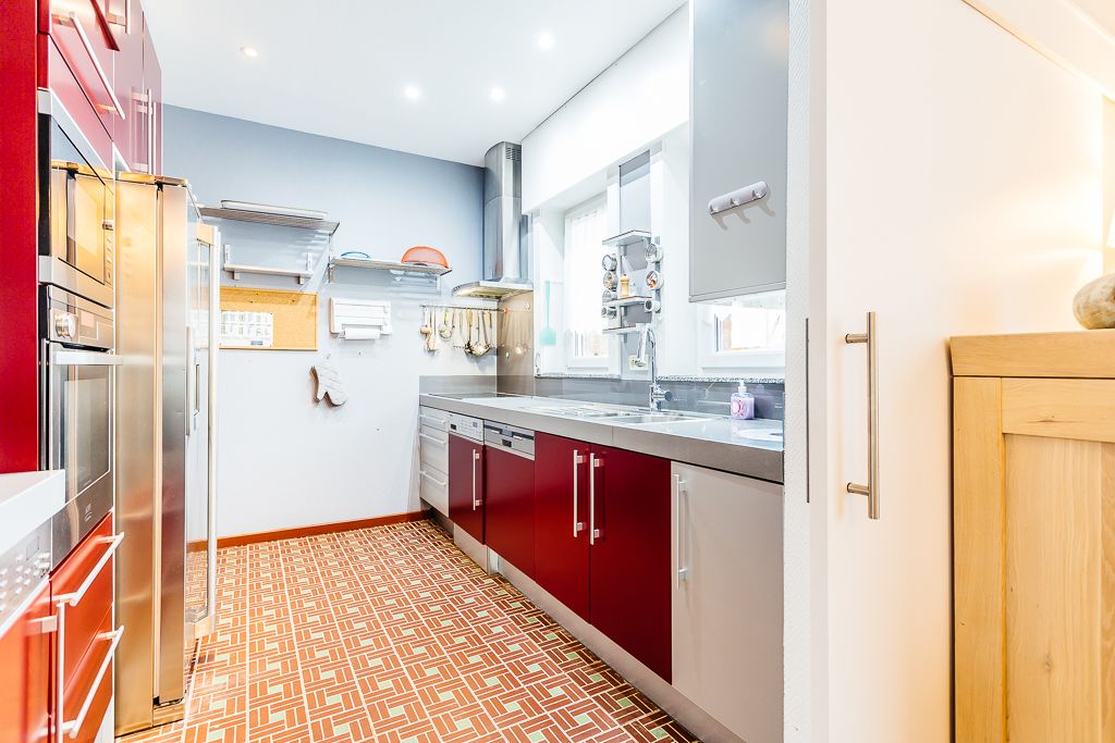 Une cuisine moderne avec des meubles de rangement rouges, des appareils électroménagers en acier inoxydable et un revêtement de sol à motifs.