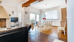 A modern living room with a black sofa, a TV, and a dining area with white chairs and a table. - Marsouins (Koksijde)