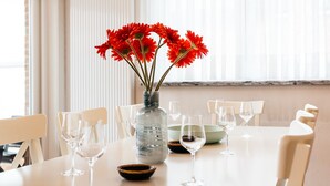 A dining table with a vase of red flowers, several wine glasses, and a water dispenser. - Marsouins (Koksijde)