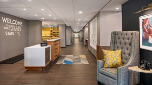A hotel lobby with a reception desk, a seating area with a tufted armchair and a patterned pillow, and a hallway leading to the back of the property. - Hampton Inn & Suites Ocean City West (Ocean City)