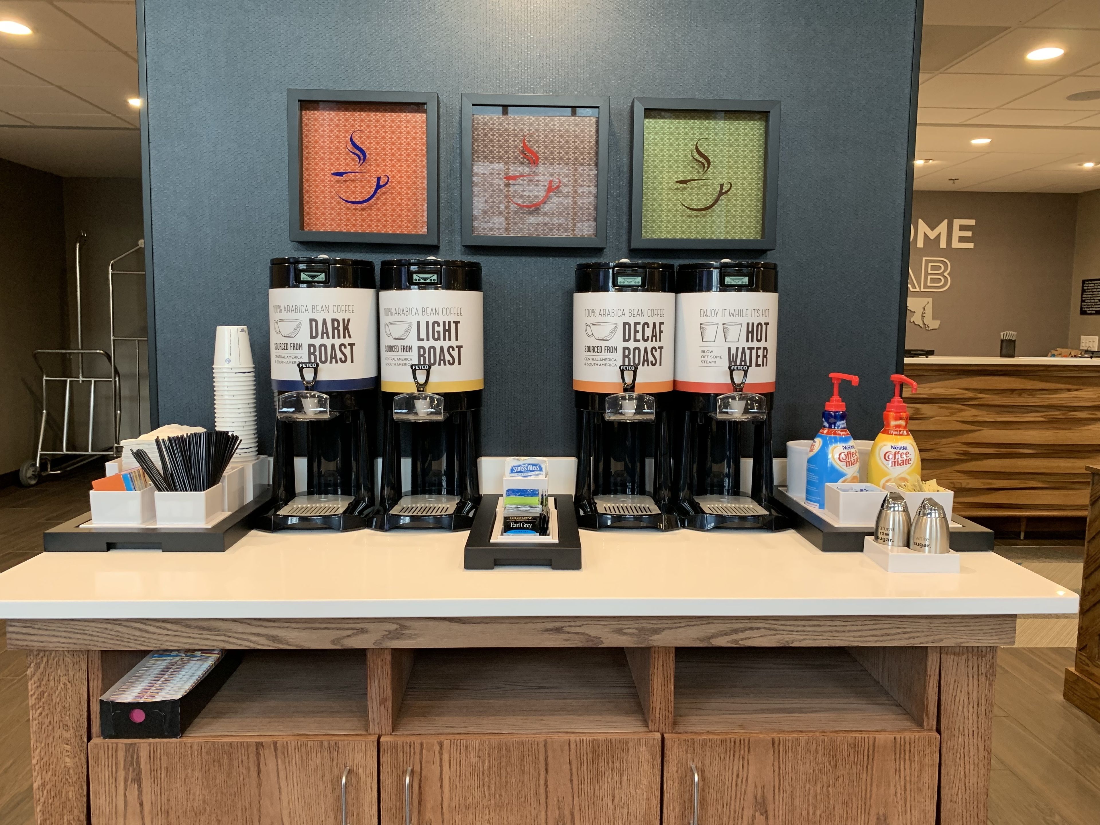 A coffee station with three coffee dispensers labeled 'Dark Roast,' 'Light Roast,' and 'Decaf Roast.' There are also condiments and napkins on the counter.