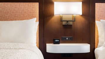 Habitación de hotel con cama, mesita de noche con reloj digital y lámpara fijada a la pared.