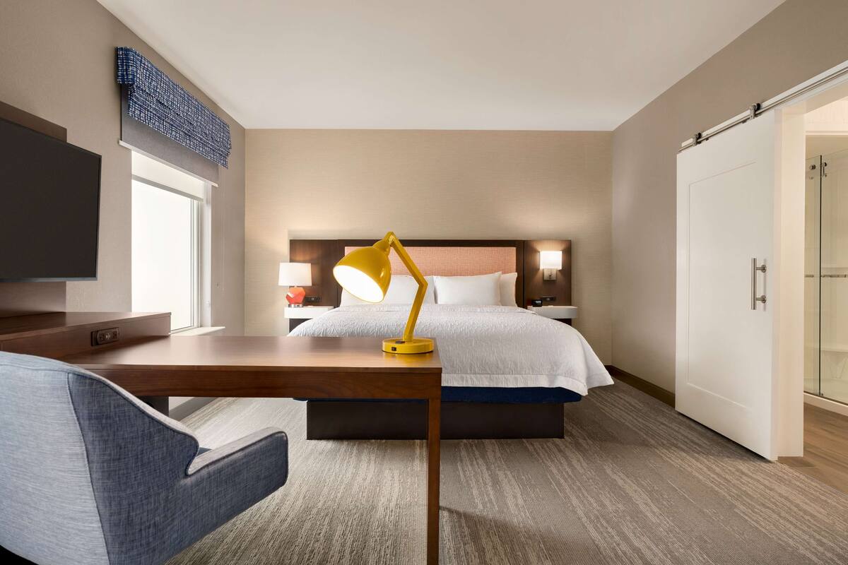 A hotel room with a bed, bedside table, lamp, TV, and a wardrobe.