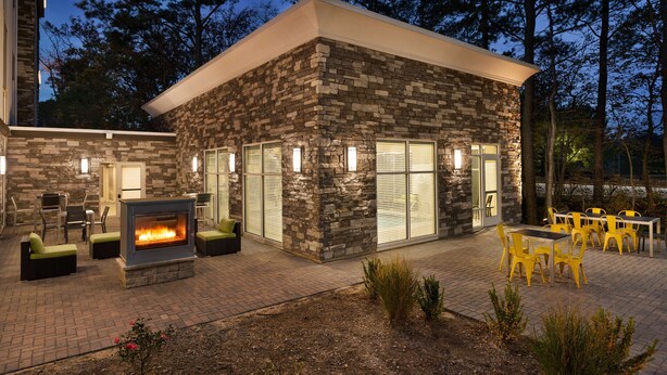 A stone building with a fire feature, outdoor seating, and a view of trees. - Hampton Inn & Suites Ocean City West (Ocean City)