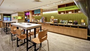 A modern restaurant with a long counter, multiple seating options, and a variety of kitchen appliances and utensils visible. - Home2 Suites by Hilton Amherst Buffalo (Buffalo)