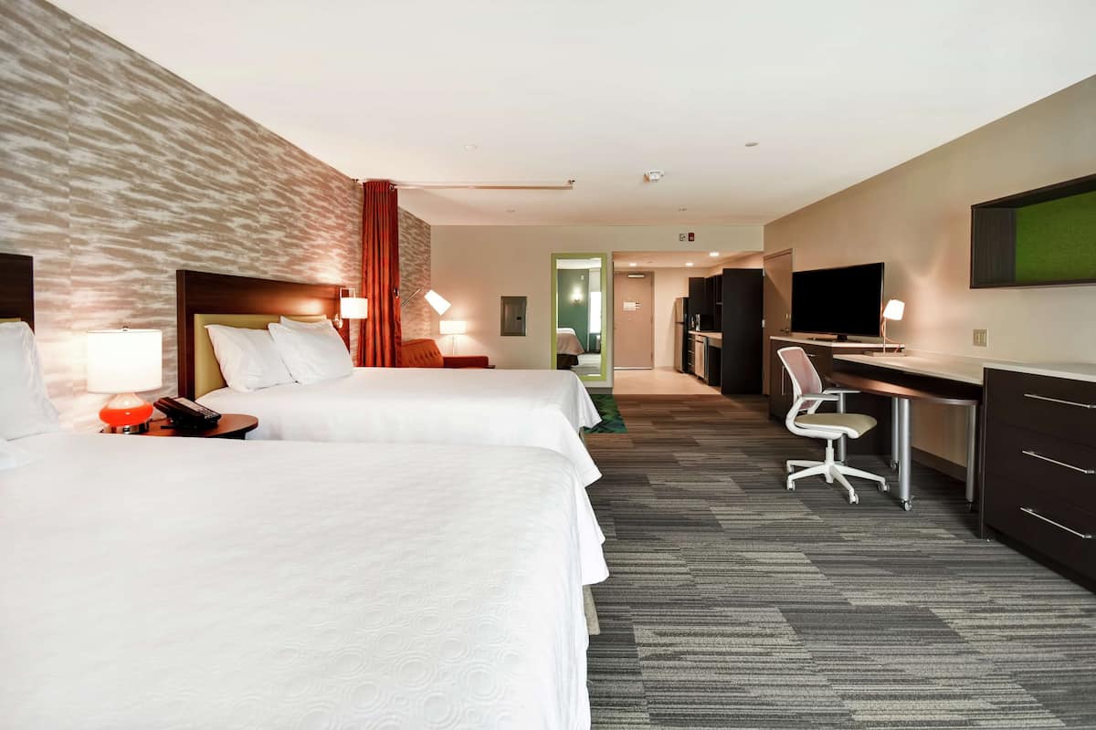 A hotel room with two beds, a desk, a TV, and a mirror.
