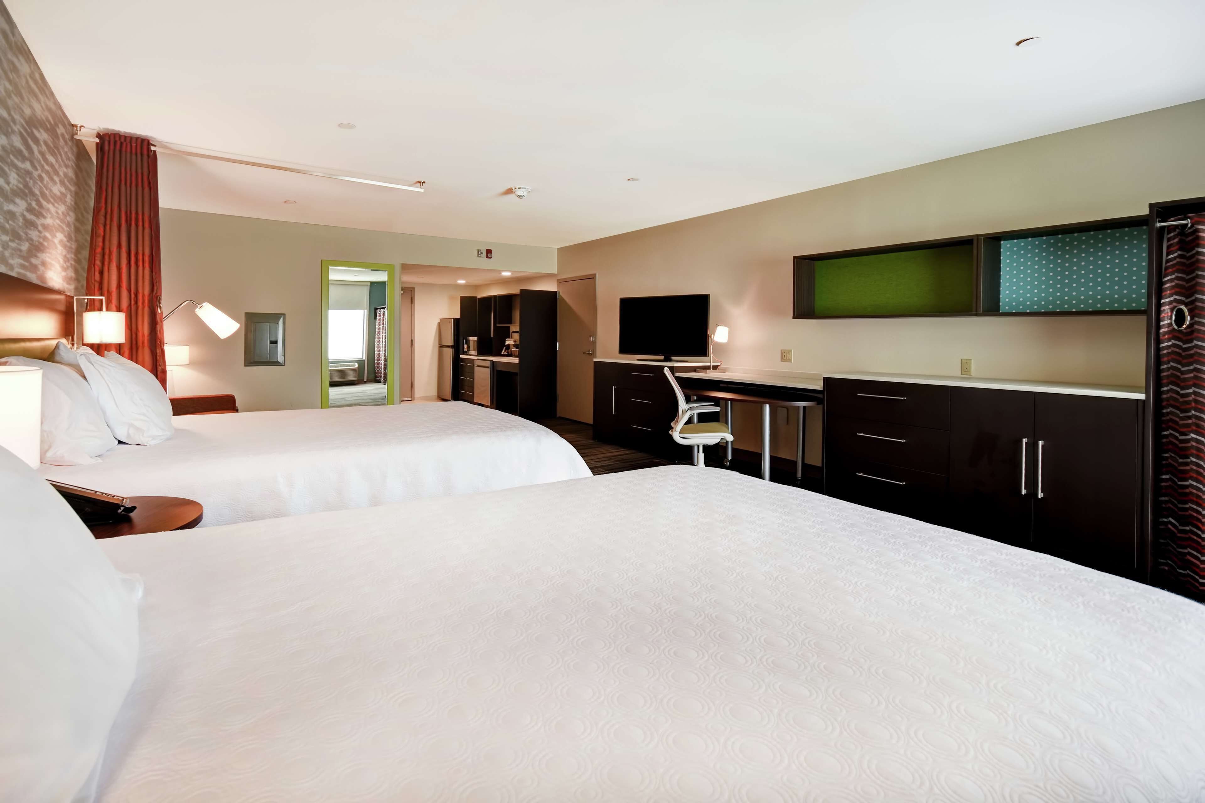 Habitación de hotel con dos camas, un escritorio, televisor y kitchenette.
